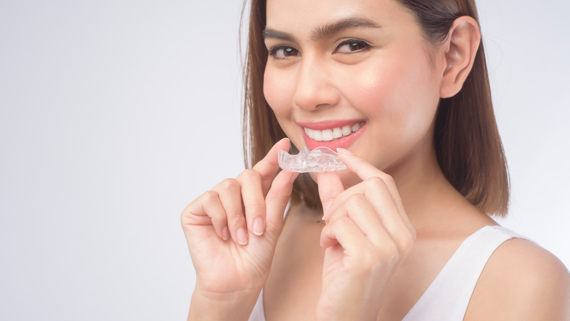Young smiling woman holding invisalign braces over white background studio,